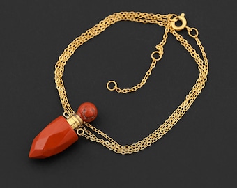 May include: A gold-colored necklace with a pendant. The pendant is a red, faceted, bullet-shaped bottle with a round, red stopper. The necklace has a triple-strand chain and a clasp.
