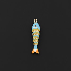 May include: A fish-shaped pendant featuring a gold-tone metal skeleton layered with light blue enamel sections. The head includes a small dark red circular accent, and the tail is finished with a white and orange enamel tip.