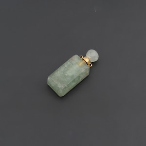 May include: A rectangular, pale green stone pendant shaped like a small bottle. It features a gold-colored metal neck and a matching pale green stone stopper. Two small gold-colored metal loops are attached to the neck of the bottle pendant.