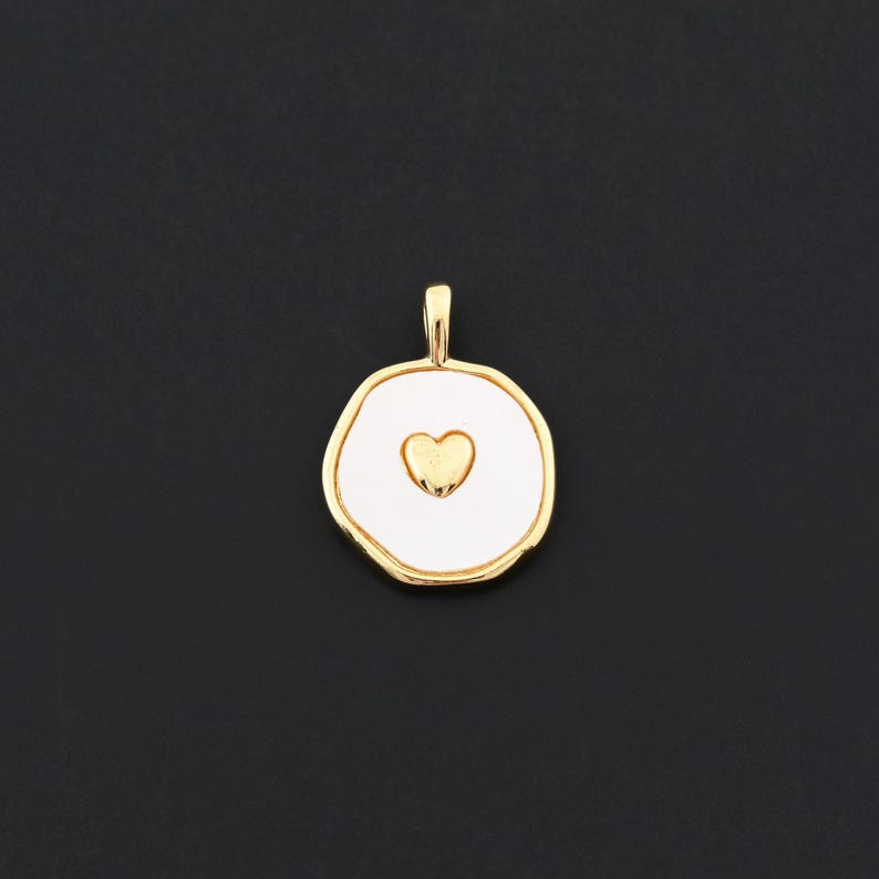 Puede incluir: Colgante dorado con centro de esmalte blanco y dise&ntilde;o de coraz&oacute;n dorado. El colgante tiene una forma irregular y org&aacute;nica y un peque&ntilde;o lazo en la parte superior para una cadena. El fondo es negro s&oacute;lido.
