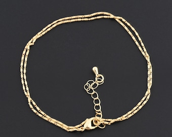 May include: A delicate gold-colored anklet with a double-strand design. The anklet features a small lobster clasp and an adjustable chain for a comfortable fit. The anklet is approximately 9 inches in length, with an additional 2 inches of adjustable chain.