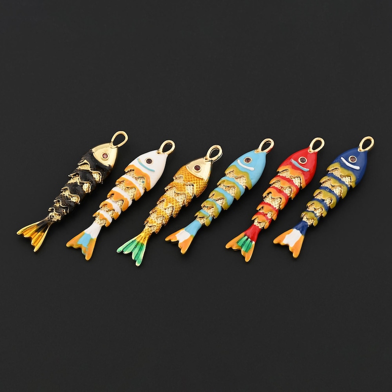 May include: Six fish-shaped pendants arranged in a row, each featuring a gold-tone textured body with colorful enamel accents on the head and tail. The colors include black, white, yellow, light blue, red, and dark blue, all with a small loop.