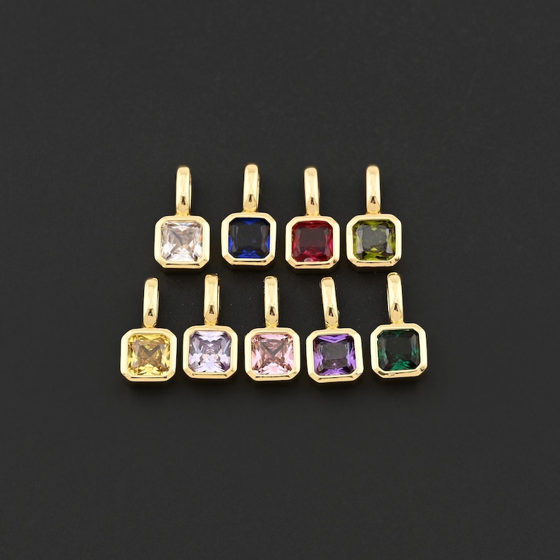 May include: A collection of nine gold-toned pendants, each featuring a square-cut gemstone in a different color. The gemstones include clear, blue, red, green, yellow, lavender, pink, purple, and dark green. The pendants are arranged on a black background.