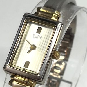 May include: A Citizen Quartz wristwatch with a rectangular gold and silver-toned face. The watch has a silver-toned band and gold accents. The watch face displays the Citizen Quartz logo.