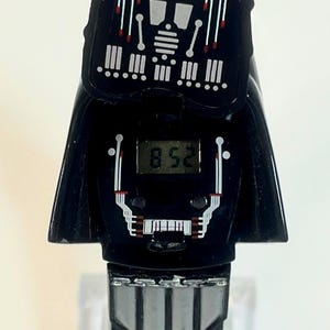 Pu&ograve; includere: Orologio digitale nero con design di Darth Vader. Il quadrante mostra l'ora 8:52. Il cinturino &egrave; nero con fibbia e dettagli argentati. Un oggetto da collezione.