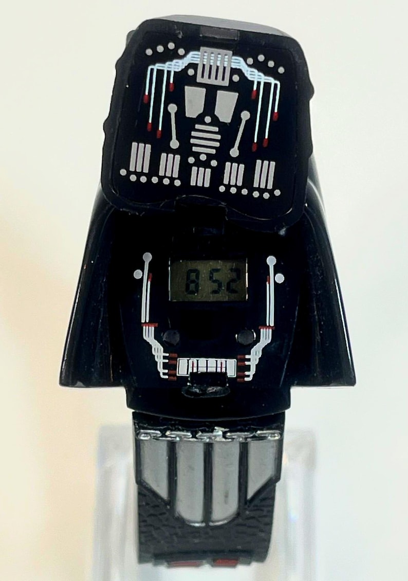 Pu&ograve; includere: Orologio digitale nero con design di Darth Vader. Il quadrante mostra l'ora 8:52. Il cinturino &egrave; nero con fibbia e dettagli argentati. Un oggetto da collezione.