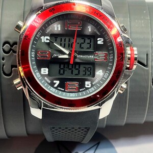 Peut inclure: Montre num&eacute;rique noire et argent&eacute;e avec une lunette rouge. Le cadran affiche l'heure et comporte plusieurs boutons. Le mot "CHYME" est imprim&eacute; sur le cadran. Le bracelet est en caoutchouc noir.