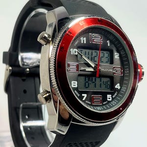 Peut inclure: Une montre num&eacute;rique noire et argent&eacute;e avec une lunette rouge. La montre a un bracelet en caoutchouc noir et affiche l'heure num&eacute;riquement. Le cadran comprend le texte "LIGHT", "JAPAN" et "STRUCTURE".