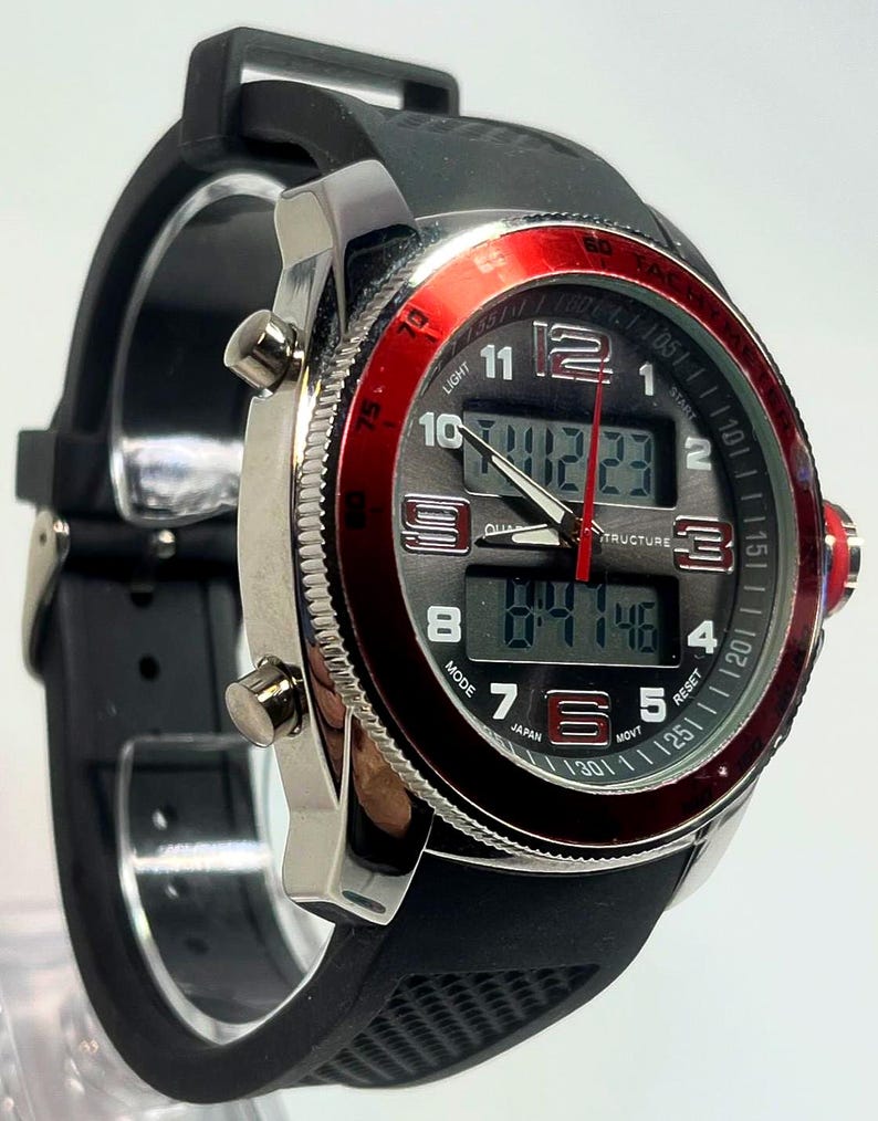 Peut inclure: Une montre num&eacute;rique noire et argent&eacute;e avec une lunette rouge. La montre a un bracelet en caoutchouc noir et affiche l'heure num&eacute;riquement. Le cadran comprend le texte "LIGHT", "JAPAN" et "STRUCTURE".
