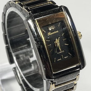May include: A rectangular wristwatch with a black face and gold-tone accents. The watch features the brand name "Ronica" and the word "Quartz". The watch band is silver and gold-tone. The watch is marked "Japan" and "Movt".