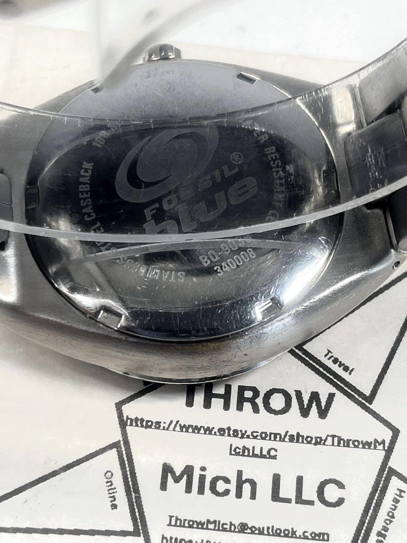 May include: A stainless steel Fossil Blue watch with a blue face. The watch has a silver band and the words "Fossil Blue" are visible on the watch face. The caseback reads "Stainless Steel Caseback" and "Water Resistant".