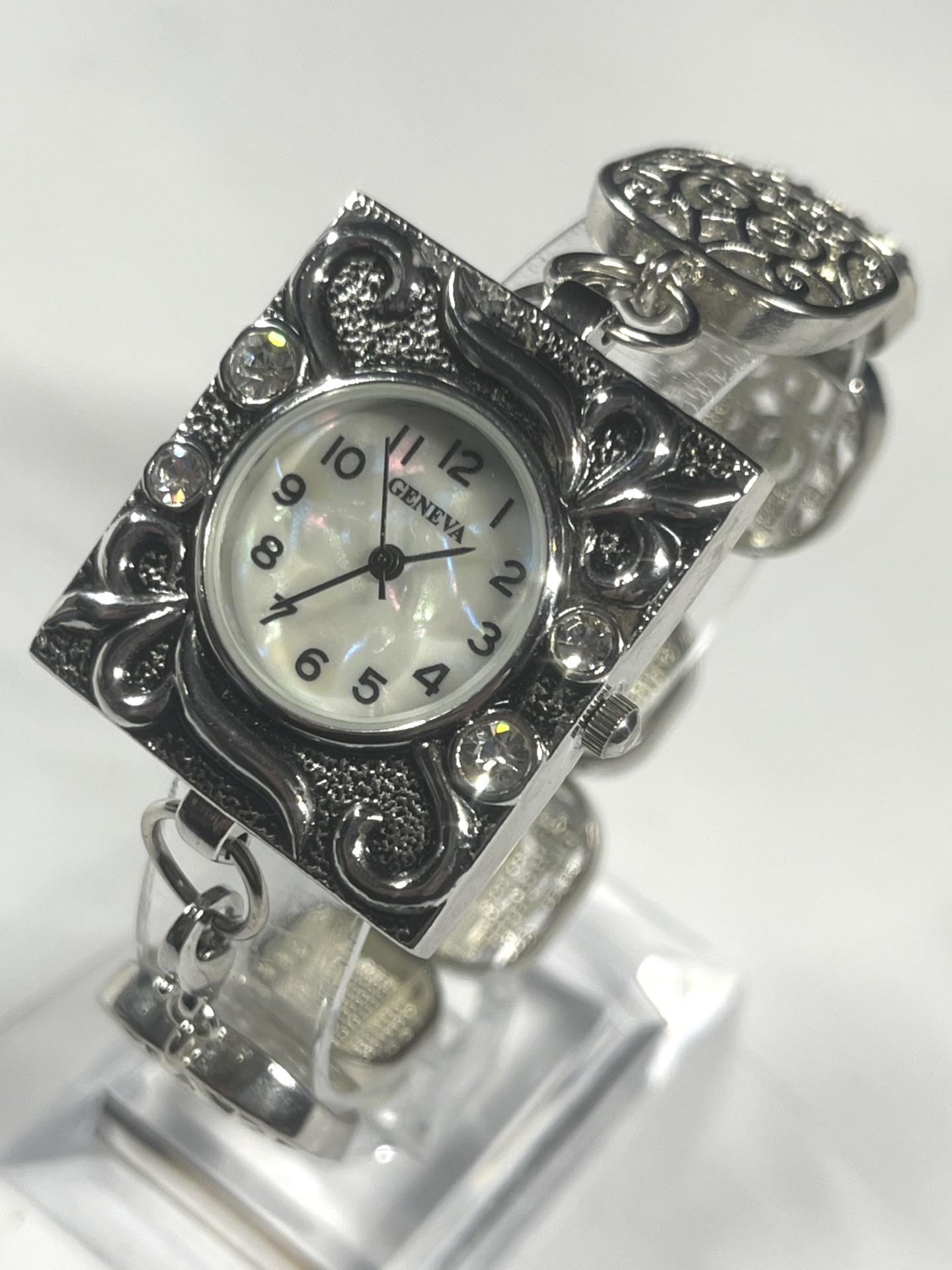 Geneva Quartz watch with an ornate square silver tone case with rhinestones on a seven segment stretch band and a new battery