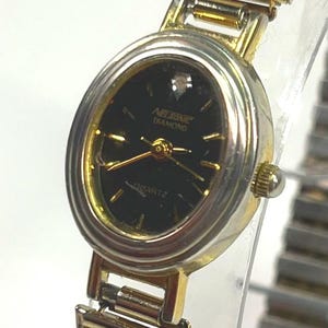 May include: A gold-toned wristwatch with a black oval face. The watch features gold hands and hour markers, with the text "NELSONIC DIAMOND QUARTZ" on the face. The watch band is also gold-toned.