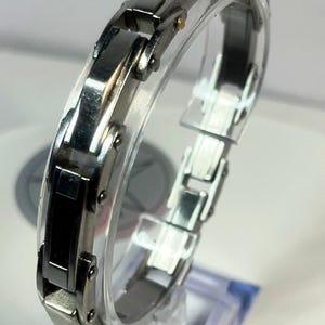 May include: A silver-toned bracelet with black rectangular accents. The bracelet is made of linked metal segments and is displayed on a clear stand. The design is modern and sleek, suitable for everyday wear.