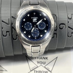 May include: A silver Fossil Blue wristwatch with a dark blue face and multiple subdials. The watch has a tachymeter bezel and a stainless steel band. The watch is displayed on a gray sizing tool. The text "THANK YOU" is visible.
