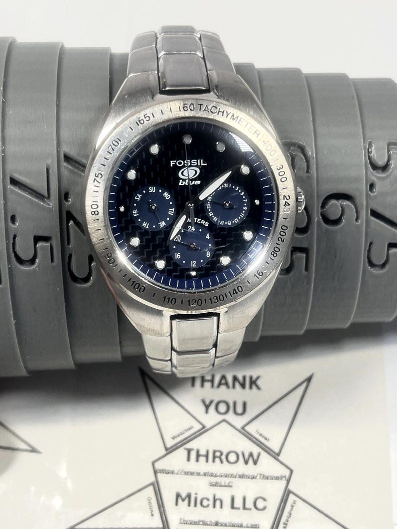 May include: A silver Fossil Blue wristwatch with a dark blue face and multiple subdials. The watch has a tachymeter bezel and a stainless steel band. The watch is displayed on a gray sizing tool. The text "THANK YOU" is visible.
