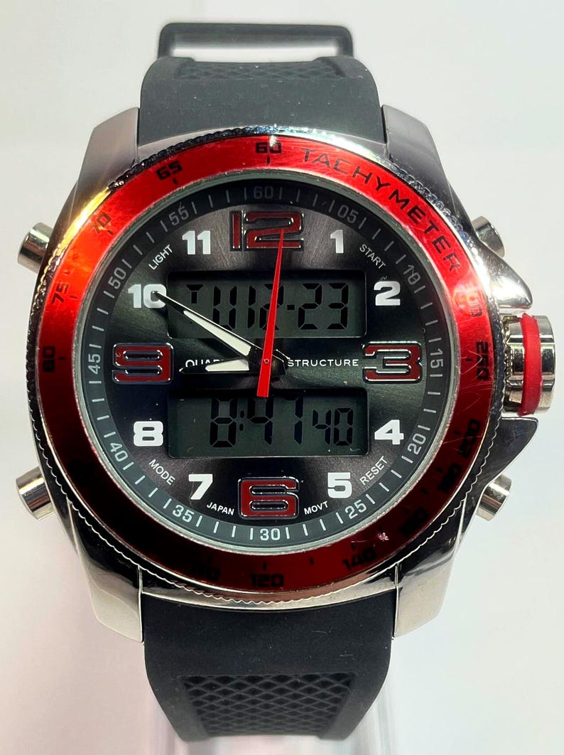 Peut inclure: Une montre num&eacute;rique argent&eacute;e avec un bracelet noir et une lunette rouge. Le cadran affiche l'heure et d'autres fonctions. La montre poss&egrave;de plusieurs boutons et une &eacute;chelle tachym&eacute;trique. La montre est marqu&eacute;e "JAPAN".