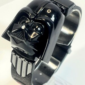 Pu&ograve; includere: Un orologio nero di Darth Vader con un design dettagliato del casco. L'orologio ha un cinturino nero con dettagli argentati e una chiusura rettangolare. Un oggetto da collezione.
