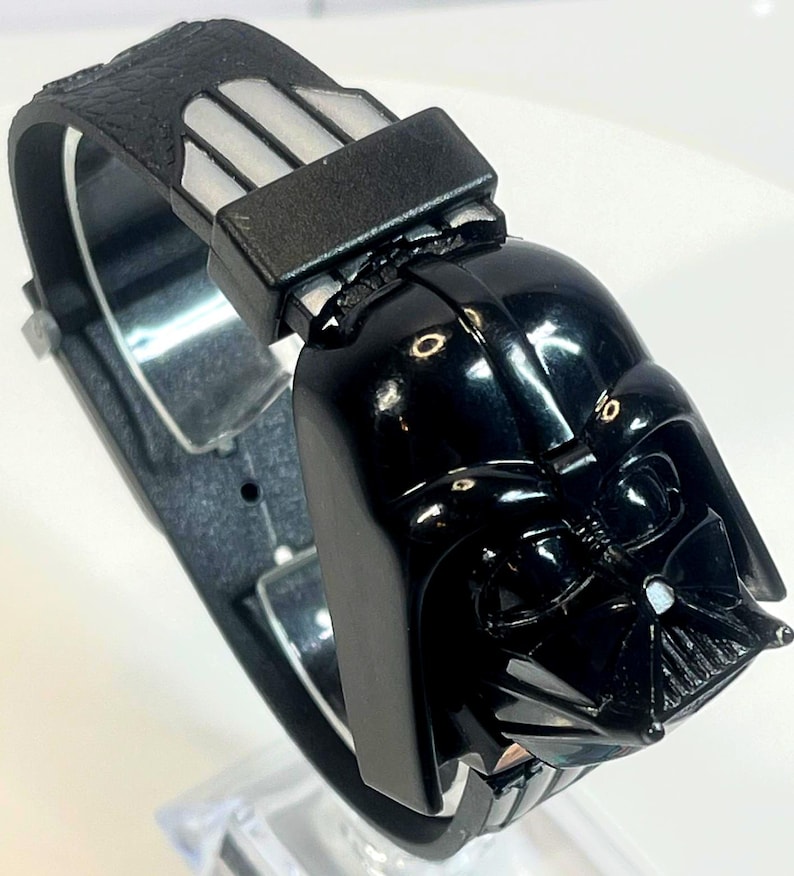 Pu&ograve; includere: Un orologio da polso nero con un design a casco di Darth Vader. L'orologio ha un cinturino nero con un motivo strutturato e una chiusura color argento. Il casco di Darth Vader &egrave; il punto focale, con dettagli intricati.
