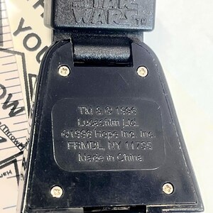 Pu&ograve; includere: Primo piano di un orologio nero di Star Wars. Il cinturino dell'orologio &egrave; nero e il quadrante dell'orologio presenta il logo di Star Wars. Il retro dell'orologio riporta la scritta "TM & &copy; 1996 Lucasfilm Ltd. &copy;1996 Hope Ind. Inc. FRMDL, NY 11735 Made in China."