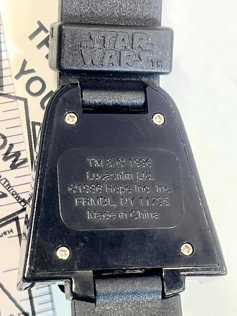 Pu&ograve; includere: Primo piano di un orologio nero di Star Wars. Il cinturino dell'orologio &egrave; nero e il quadrante dell'orologio presenta il logo di Star Wars. Il retro dell'orologio riporta la scritta "TM & &copy; 1996 Lucasfilm Ltd. &copy;1996 Hope Ind. Inc. FRMDL, NY 11735 Made in China."