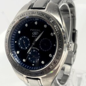 May include: A stainless steel Fossil watch with a dark blue face. The watch features a tachymeter bezel and multiple sub-dials. The watch face displays the brand name "Fossil" and the word "blue". The watch band is also stainless steel.