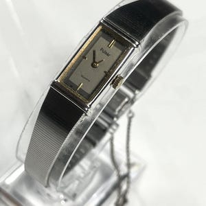 May include: A silver-toned Pulsar quartz watch with a rectangular face and a silver band. The watch face is a light champagne color with black hands and gold accents. The watch is displayed on a clear stand.