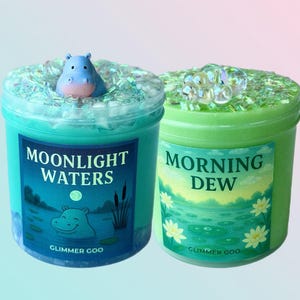 Pode incluir: Dois potes de slime Glimmer Goo. Um é azul-turquesa com uma figura de hipopótamo e as palavras "Moonlight Waters". O outro é verde com as palavras "Morning Dew". Ambos os potes têm glitter e elementos decorativos.