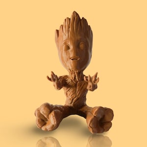 May include: A brown figurine of the character Groot from the Guardians of the Galaxy franchise. The figure is in a seated position with arms outstretched. The figurine is made of a textured material and has a detailed facial expression.