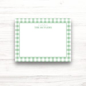 Puede incluir: Una tarjeta de papelería rectangular con un centro blanco y un borde de cuadros verde claro. El texto "a note from THE BUTLERS" está impreso en el centro de la tarjeta. La tarjeta está sobre un fondo blanco con vetas de madera.