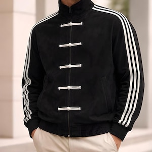 Può includere: Giacca nera con strisce bianche sulle maniche e colletto alto. La giacca ha una chiusura a zip e bottoni bianchi. Pantaloni beige.