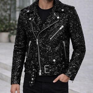May include: Black sequin motorcycle jacket with silver zippers, a notched collar, and a buckle belt. The jacket has a classic biker style with a fitted silhouette and multiple pockets. The jacket is a statement piece, perfect for adding a touch of glamour to any outfit.