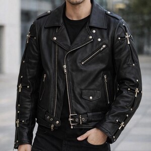 Puede incluir: Chaqueta de cuero negra de estilo motero con cremalleras, broches y cinturón plateados. La chaqueta presenta cruces doradas decorativas en las mangas y los hombros. Un estilo motero clásico con una estética moderna y atrevida.