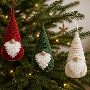 May include: Three hanging ornaments shaped like gnomes with tall pointed hats in red, dark green, and cream. Each gnome features a round beige nose and a long white crocheted beard with looped edges, suspended by a thin matching string loop.
