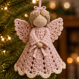 May include: A crocheted angel ornament featuring a light pink dress with a scalloped cream-colored hem, light brown yarn hair, a small pink bow on the head, and a matching pink ribbon tied at the waist, suspended by a pink string loop.