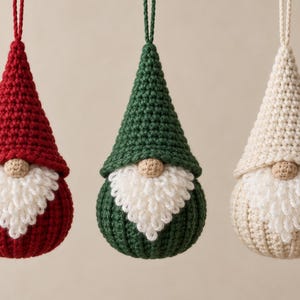 May include: Three crochet gnome ornaments hanging by loops. Each gnome features a pointed hat, a round beige nose, and a textured white beard. The gnomes are colored in solid red, dark green, and cream, with a consistent ribbed stitch pattern.