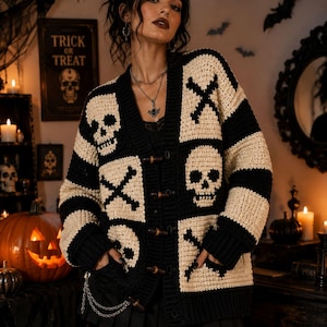 May include: A black and cream crochet cardigan featuring a repeating pattern of skulls and crossbones. The garment has a V-neckline, long sleeves, ribbed cuffs, and is fastened down the front with four brown toggle buttons. It includes two front pockets.