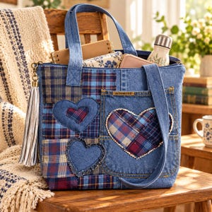 May include: A blue denim tote bag featuring a patchwork design of blue and red plaid fabric squares. The bag is decorated with two denim heart-shaped appliqués and a large front pocket with a label reading SCHMIDT. A long white tassel hangs from the side.
