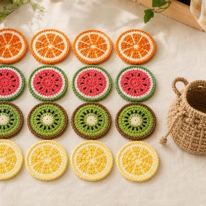 May include: A set of sixteen round, crocheted coasters featuring fruit slice designs, including orange, watermelon, kiwi, and lemon patterns, arranged in a grid alongside a small, tan, woven drawstring basket with two side handles.