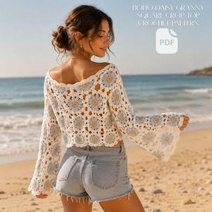 May include: A long-sleeved crochet crop top featuring a repeating pattern of white, light blue, and yellow daisy granny squares. The garment has a wide neckline and flared sleeves. Text in the image reads: BOHO DAISY GRANNY SQUARE CROP TOP CROCHET PATTERN PDF.