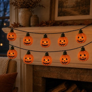Puede incluir: Una guirnalda de diez luces de calabaza iluminadas dispuestas en dos filas horizontales. Cada calabaza naranja presenta una superficie texturizada, un tallo verde y una cara negra tallada con ojos triangulares y una boca dentada.