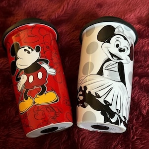 Pu&ograve; includere: Due tazze da viaggio con personaggi Disney. Una tazza &egrave; rossa con un design di Topolino, e l'altra &egrave; bianca con un design di Minnie. Entrambe le tazze hanno coperchi neri e sono di forma cilindrica.