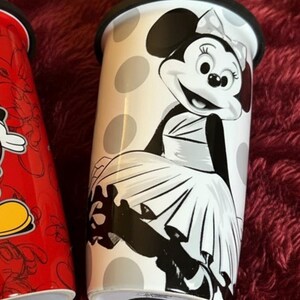 Pu&ograve; includere: Un bicchiere da viaggio bianco con coperchio nero, con Minnie Mouse in un design a pois bianchi e neri. Il bicchiere ha un'illustrazione in bianco e nero di Minnie Mouse. L'altro bicchiere &egrave; rosso con un design di Topolino.