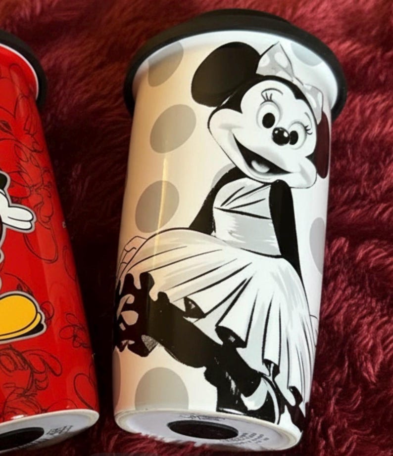 Pu&ograve; includere: Un bicchiere da viaggio bianco con coperchio nero, con Minnie Mouse in un design a pois bianchi e neri. Il bicchiere ha un'illustrazione in bianco e nero di Minnie Mouse. L'altro bicchiere &egrave; rosso con un design di Topolino.