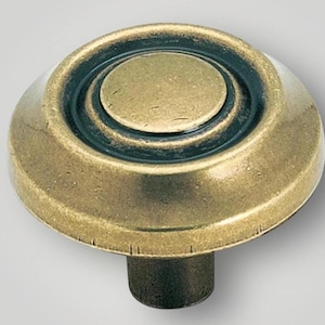 Puede incluir: Primer plano de un tirador de armario de latón antiguo. El pomo tiene un diseño circular con anillos concéntricos y un acento verde oscuro. El vástago es de color bronce oscuro. Adecuado para la restauración de muebles. Diámetro aproximado de 3,8 cm.