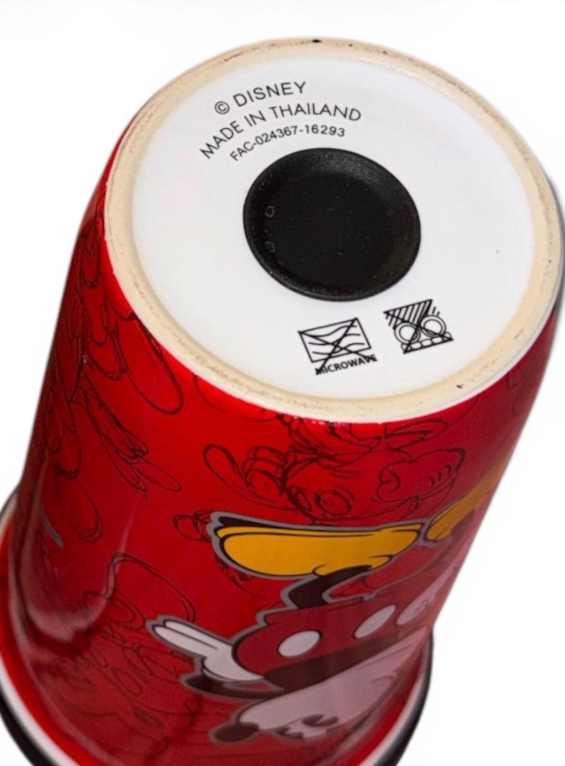 Pu&ograve; includere: Bicchiere in ceramica rosso con Topolino e altri personaggi Disney. Il fondo del bicchiere riporta la scritta "&copy; DISNEY MADE IN THAILAND" e simboli per microonde.