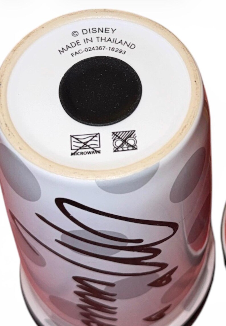Pu&ograve; includere: Una tazza Disney in ceramica bianca con base nera. La tazza presenta un design di ovali grigi e rossi e linee astratte nere. Il fondo della tazza riporta la scritta "DISNEY MADE IN THAILAND" e simboli per microonde.