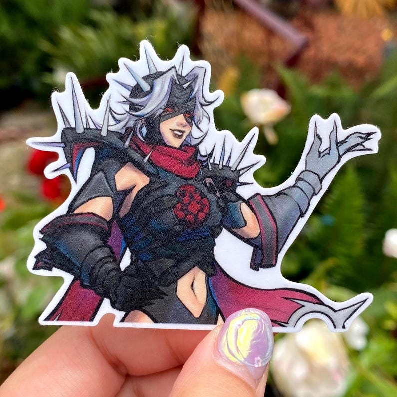 May include: A sticker featuring a stylized illustration of a character in black armor with a red scarf and accents. The character has white hair, a blindfold, and a spiked crown. The sticker is held by a hand.