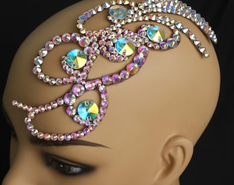 May include: A decorative headpiece with iridescent rhinestones and large, colorful crystals. The design features swirling patterns of small rhinestones and larger, multi-colored crystals. The headpiece is set against a neutral background.