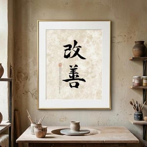 以下が含まれることがあります： テクスチャ加工されたベージュの背景に、黒い日本語の書道文字が描かれた額装アートプリント。小さな赤い印章と縦書きのテキストが含まれており、細いゴールドのフレームに収められた、すっきりとしたデザインの作品です。